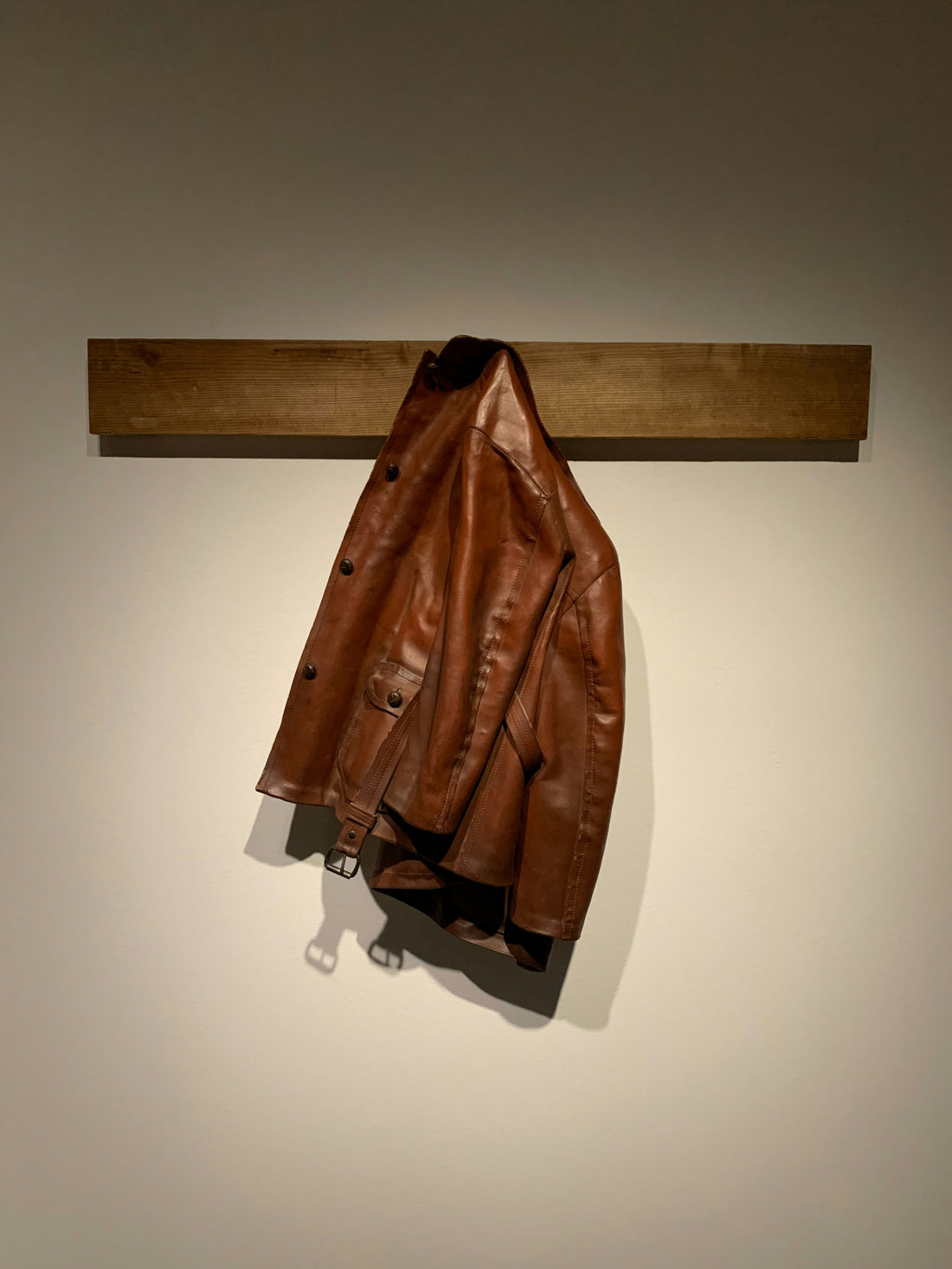 Brown leather jacket hanging on a wooden wall hook